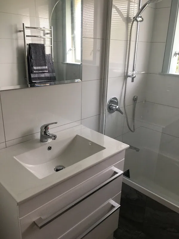 After renovation: modern bathroom with white vanity, large mirror, frameless shower enclosure and white subway tiles
